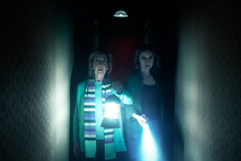 Elise Rainier y Gemma en el pasillo oscuro Elise Rainier acompañada de Gemma recorriendo un pasillo oscuro iluminado únicamente por una linterna de gas y una linterna de mano.
