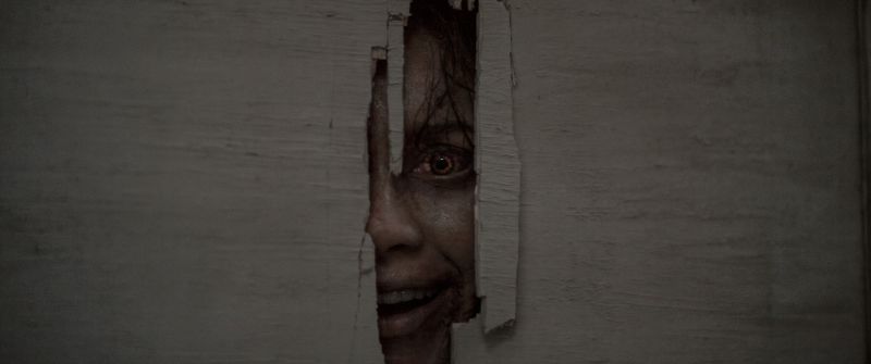 Una entidad poseída observa a través de una abertura en una pared, anticipando uno de los momentos de mayor tensión del filme.