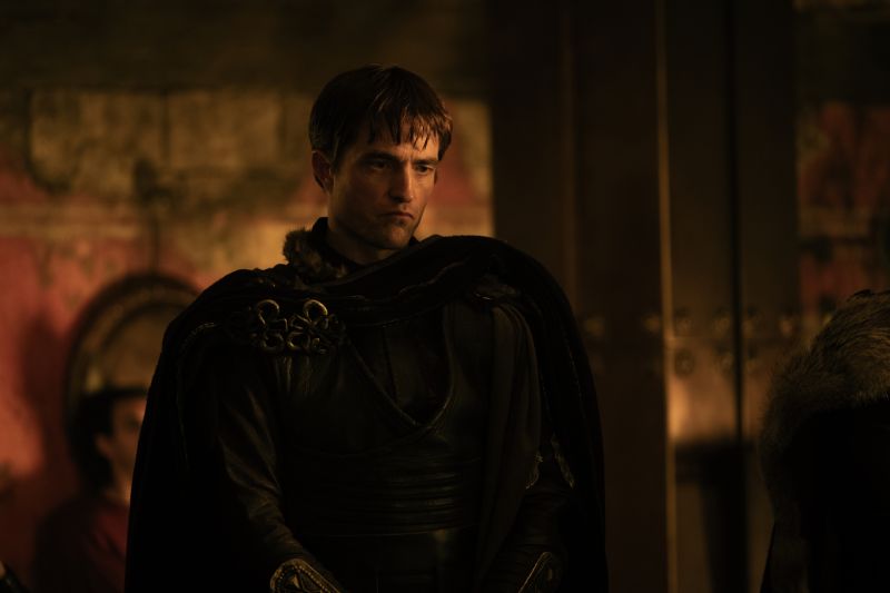Primer plano medio de Robert Pattinson caracterizado como Antínoo en una escena nocturna/interior luciendo vestimenta de cuero y capas obscuras en la película La Odisea.