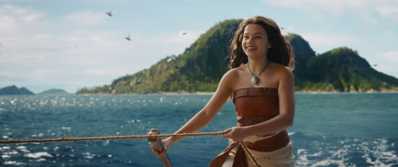 Moana sostiene una cuerda sobre una embarcación en medio del océano con islas al fondo.