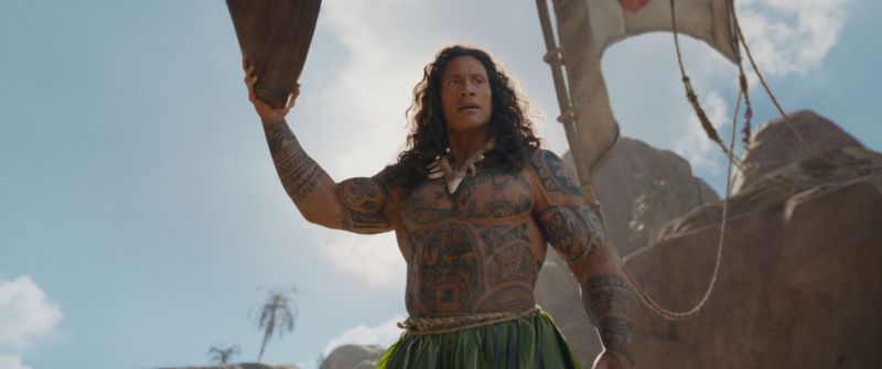 Maui aparece con tatuajes polinesios y un arma ceremonial en un entorno rocoso.