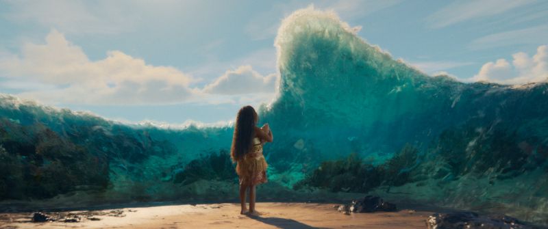 Moana observa una ola monumental que se eleva frente a ella en una playa tropical.