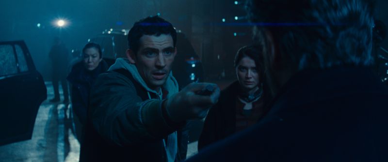 Escena nocturna con varias personas en un entorno urbano iluminado en tonos azules.