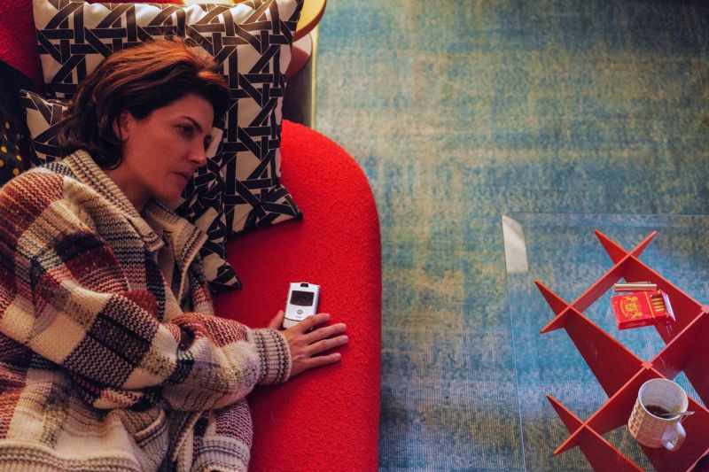 Persona recostada en sofá rojo con objetos personales alrededor.