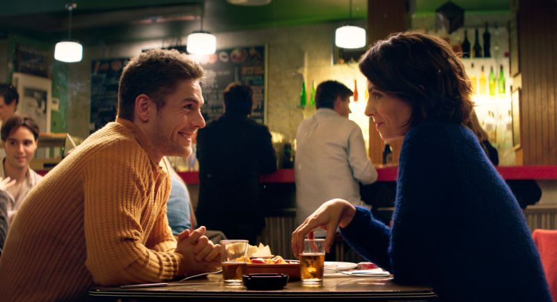 Dos personas conversando en un bar cálido con bebidas en la mesa.