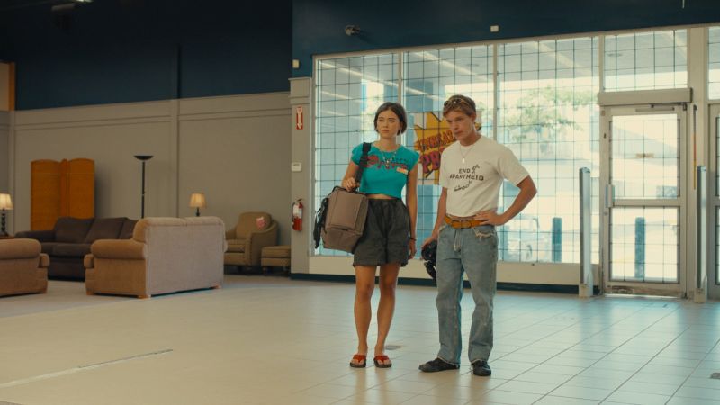 Backrooms — Rutina y frustración Dos personas en un showroom iluminado con muebles y ventanales.