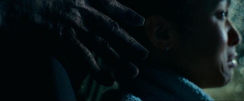 Mano espectral iluminada tratando de alcanzar a una mujer aterrada dentro de un vehículo bajo atmósfera de suspenso.
