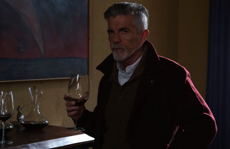 Retrato — La vida es Persona mayor sosteniendo una copa de vino en un interior cálido.
