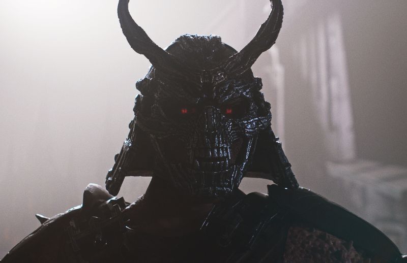 Figura con casco oscuro y cuernos iluminado por ojos rojos en un ambiente lleno de niebla.
