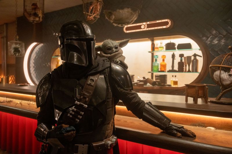 Cantina — The Mandalorian and Grogu Mandaloriano en una barra con Grogu sobre su hombro.