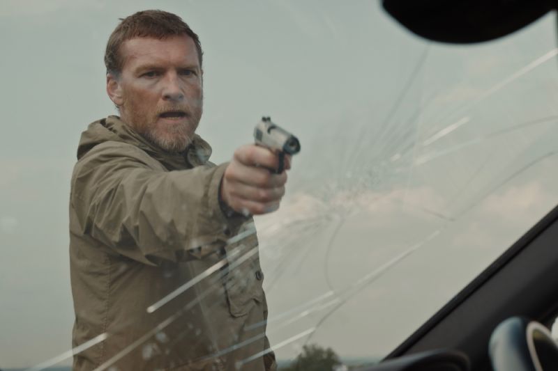 Zona de riesgo — Momento crítico Persona apuntando un arma hacia un parabrisas roto.