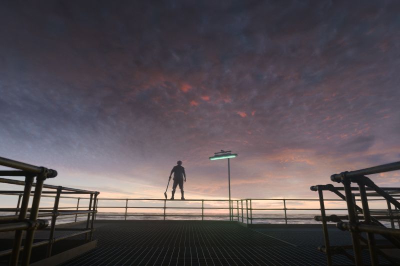 Silueta de un personaje sosteniendo una pala sobre una plataforma industrial en el mar al atardecer bajo un cielo en tonos violeta y naranja.