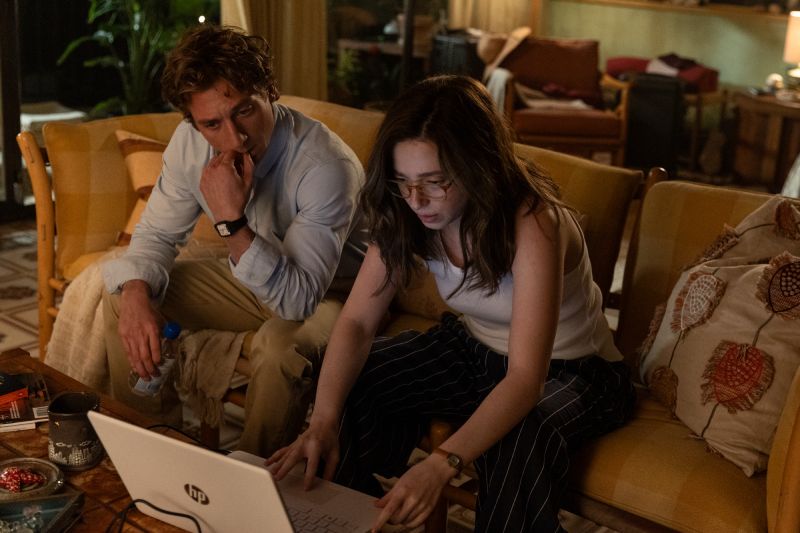 Revisión de Archivos Secretos Jeremy Allen White pensativo sosteniendo documentos y Mikey Madison operando una computadora en una sala de estar.