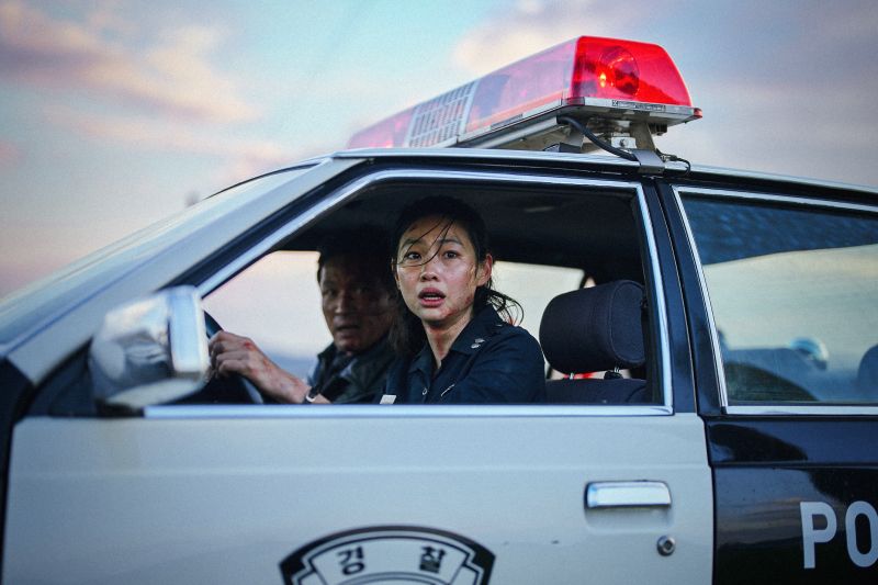Hoyeon e Hwang Jung-min dentro de una patrulla policial observando con tensión hacia afuera durante una persecución.