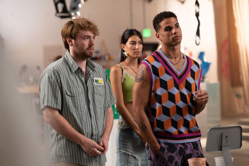 Cooper Hoffman con camisa a rayas junto a otros dos actores en un estudio o taller artístico.