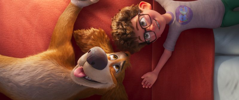 Charlie y su Joven Dueño El perro Charlie y su joven dueño descansando felices juntos sobre una cama roja compartiendo un momento de complicidad.