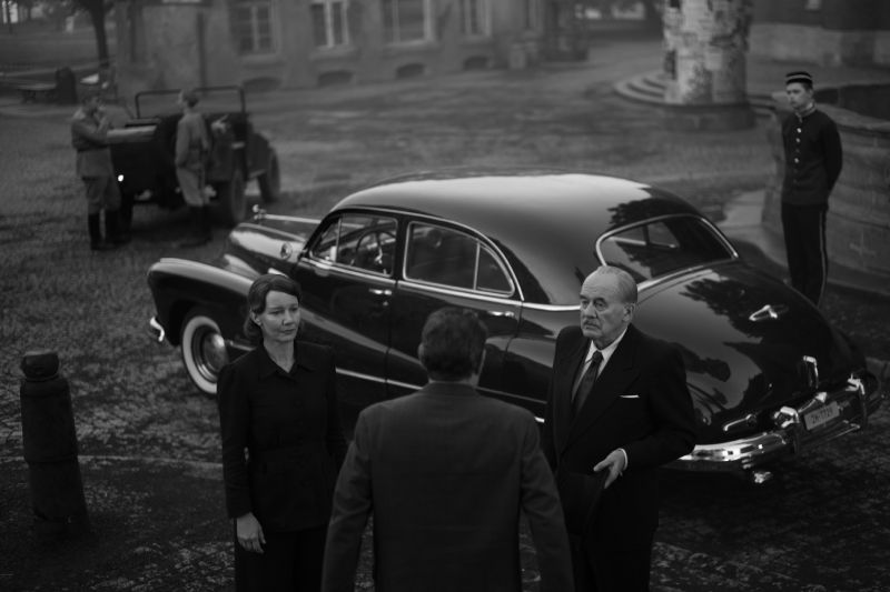 El Regreso de Thomas Mann a Alemania Thomas Mann y su acompañante junto a un automóvil clásico negro en una plaza pública europea durante la posguerra.