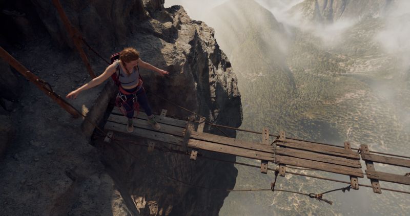 Cruzando el puente colgante sobre el abismo Una escaladora de pie con los brazos abiertos sobre las maderas inestables de un puente colgante sobre un abismo.