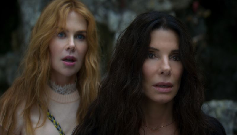 Sandra Bullock con cabello largo y oscuro en primer plano junto a Nicole Kidman pelirroja al fondo, ambas con expresiones de asombro y preocupación mirando hacia el frente.