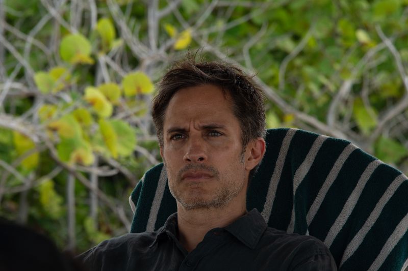 Gael García Bernal en Hombre al agua Primer plano del actor Gael García Bernal con expresión seria y pensativa sentado en una silla reclinable en un entorno natural.
