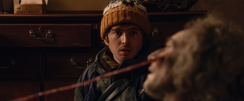 Primer plano de Bryan con un gorro tejido mirando fijamente con expresión atónita y desconcertada hacia una criatura u organismo con tentáculos que se extiende frente a él.
