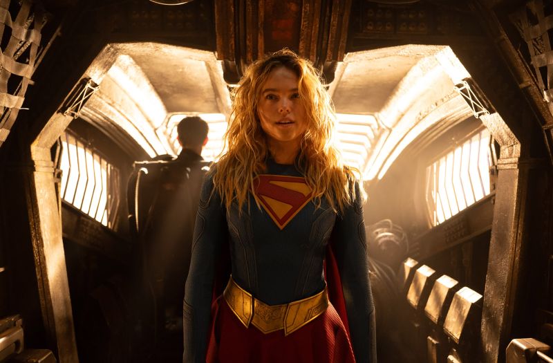 Plano frontal de Kara Zor-El con el traje de Supergirl en el pasillo de una nave espacial iluminado por una cálida luz dorada de fondo.