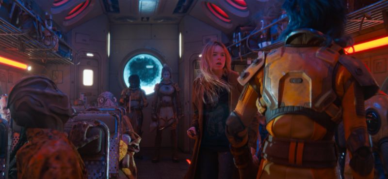 Fotograma del interior de un transporte espacial repleto de diversas criaturas e individuos alienígenas, con Kara en el centro reaccionando sorprendida.