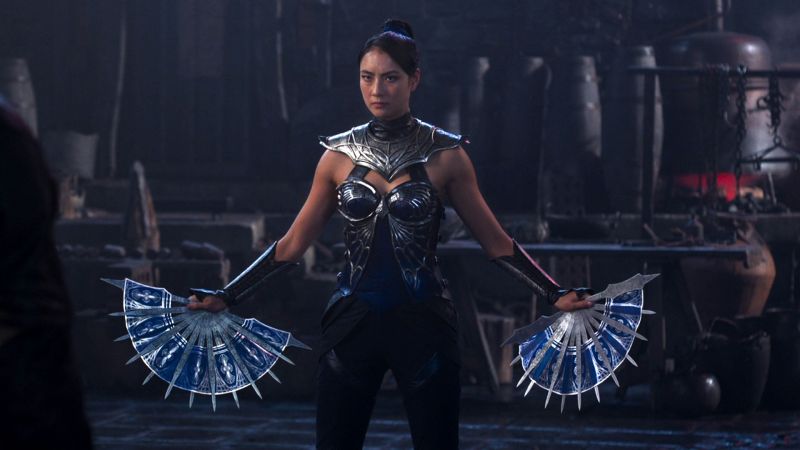 Mortal Kombat II — Kitana en la forja Kitana sosteniendo abanicos afilados en un entorno industrial iluminado tenuemente.