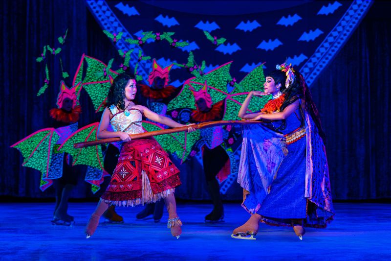 Dos intérpretes enfrentados en una coreografía inspirada en la mitología polinesia, rodeados por bailarines con alas verdes.