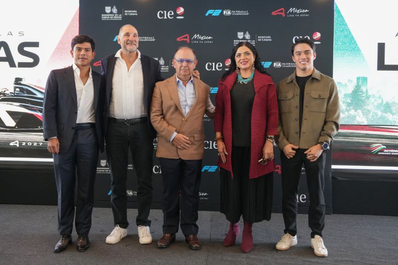 Fotografía de la conferencia de prensa con directivos y los pilotos mexicanos Rafael Villagómez y Noel León posando sonrientes sobre un escenario con el mampara promocional del evento.