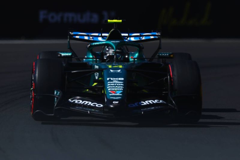 Fotografía frontal del monoplaza de Fórmula 1 de la escudería Aston Martin, conducido por el piloto español Fernando Alonso sobre el trazado del Gran Premio de España, destacando la toma aérea verde sobre el casco del conductor y la luz frontal sobre el asfalto.