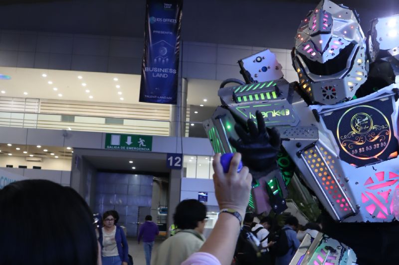 Persona interactuando con un robot humanoide iluminado con luces de colores en un evento tecnológico.