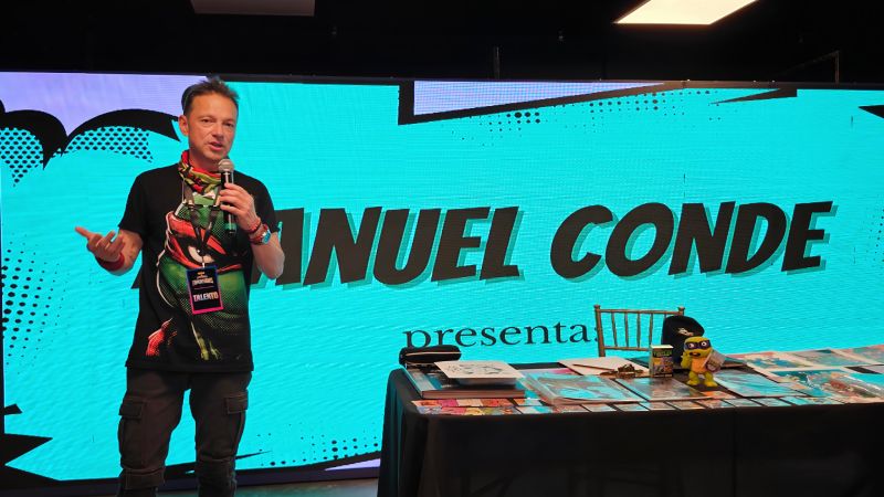 El ilustrador Manuel Conde impartiendo un taller de dibujo sobre las Tortugas Ninja frente a una pantalla gigante interactiva con su nombre.