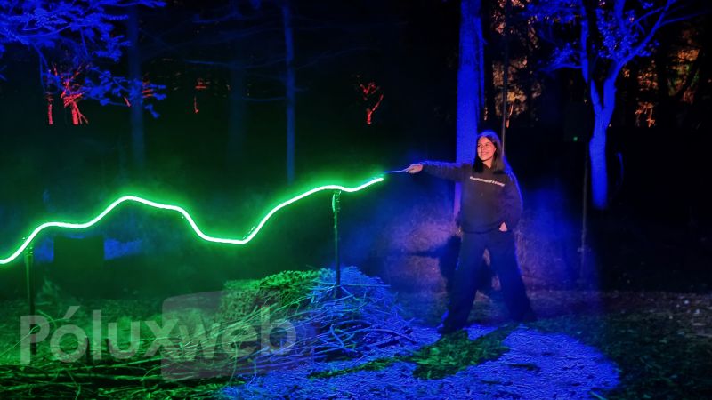 Visitante utilizando una varita mágica interactiva para encender una estela de luz verde neón a lo largo del bosque.