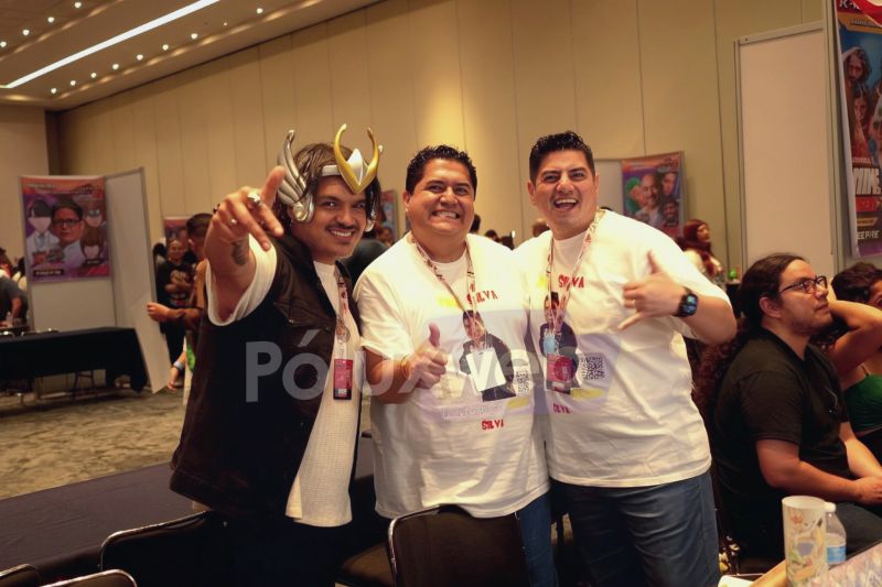 Los hermanos Silva posando sonrientes durante su convivencia en el área de invitados de AniMole 4, usando playeras conmemorativas y uno de ellos portando un casco dorado de cosplay.