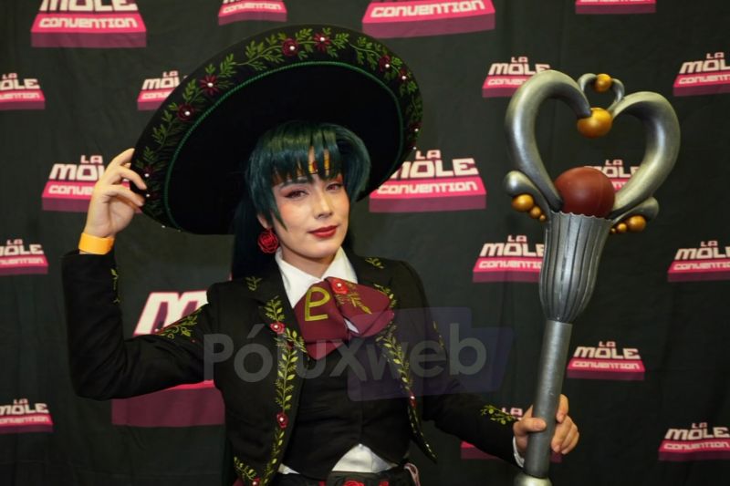 Cosplayer personificando a Sailor Pluto vestida con un traje de charro mexicano negro con bordados florales y sombrerote, sosteniendo el Cetro del Granate.