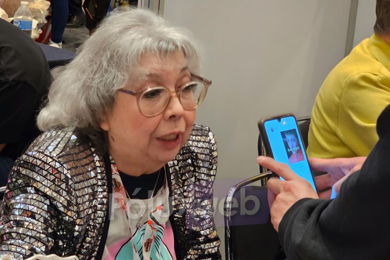 La actriz de doblaje Rocío Garcel con saco de lentejuelas brillantes conversando atentamente con un asistente mientras graba un saludo en un teléfono celular.