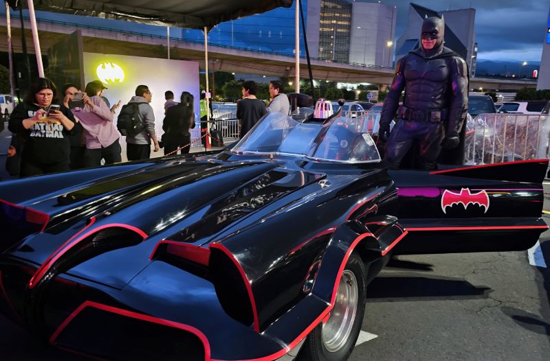 Una réplica del Batimóvil de la serie de televisión de 1966 de Adam West con un cosplayer de Batman posando junto a la puerta del conductor.