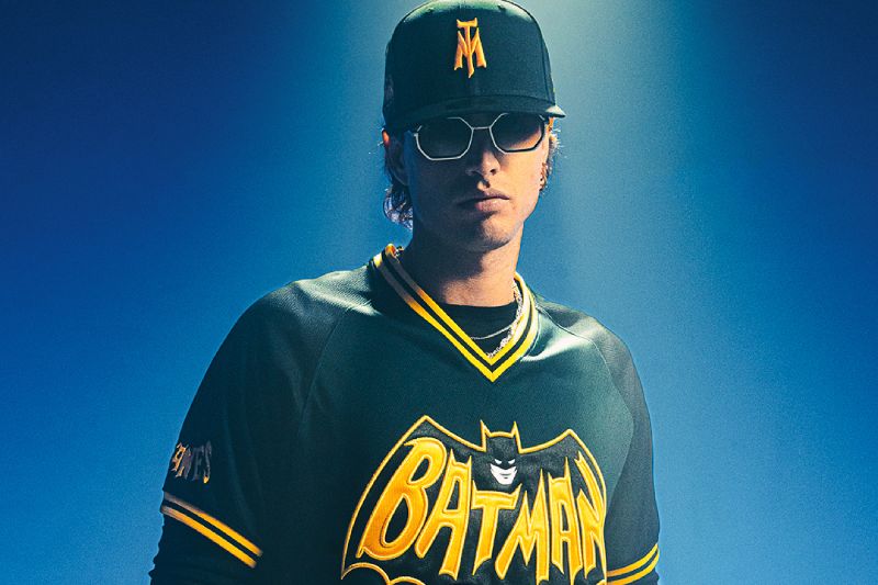 Persona con jersey y gorra inspirados en Batman, iluminado con tonos azules en un entorno oscuro.