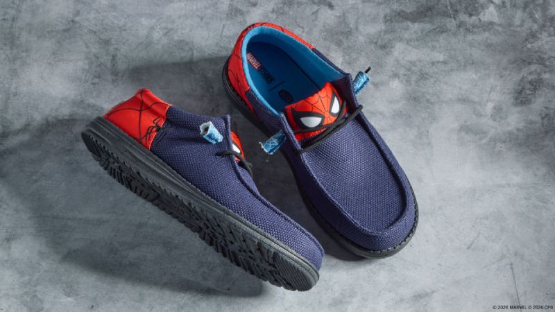 Calzado casual Wally Funk de la colección HEYDUDE x Marvel Fotografía de producto en vista superior de un par de calzado mocasín casual modelo Wally Funk en azul marino, con paneles traseros y lengüeta en rojo decorados con el diseño de la máscara y telarañas de Spider-Man sobre una superficie gris de concreto.