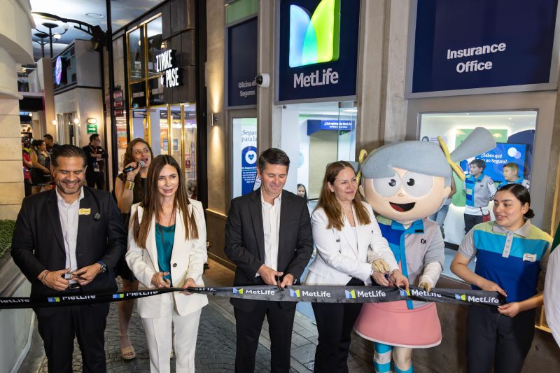 MetLife México y KidZania – Inauguración de Oficina de Seguros Grupo de personas en un evento inaugural cortando un listón frente a una oficina de seguros, acompañados por un personaje disfrazado.