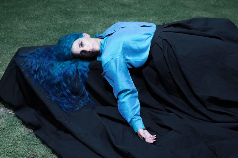 Sofía Rei se presentará en vivo en el Lunario del Auditorio Nacional Fotografía de la cantautora Sofía Rei recostada en el césped vistiendo una camisa azul turquesa y falda negra, luciendo su característico cabello largo de color azul.