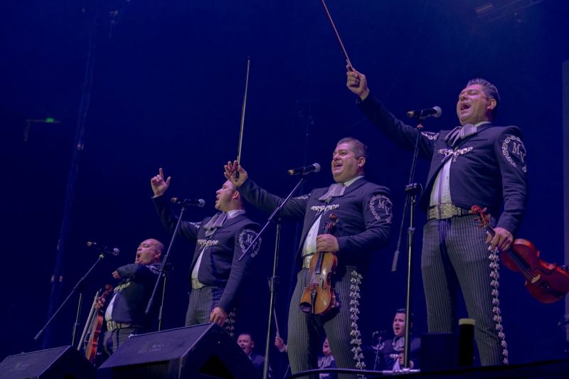 Grupo de mariachis interpretando música en escenario iluminado.