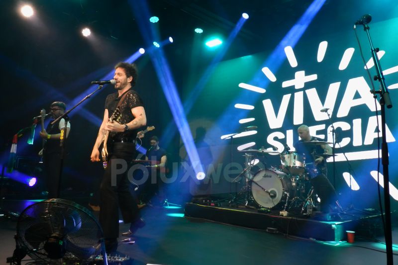 Banda completa tocando con luces azules y púrpuras y pantalla con su nombre.