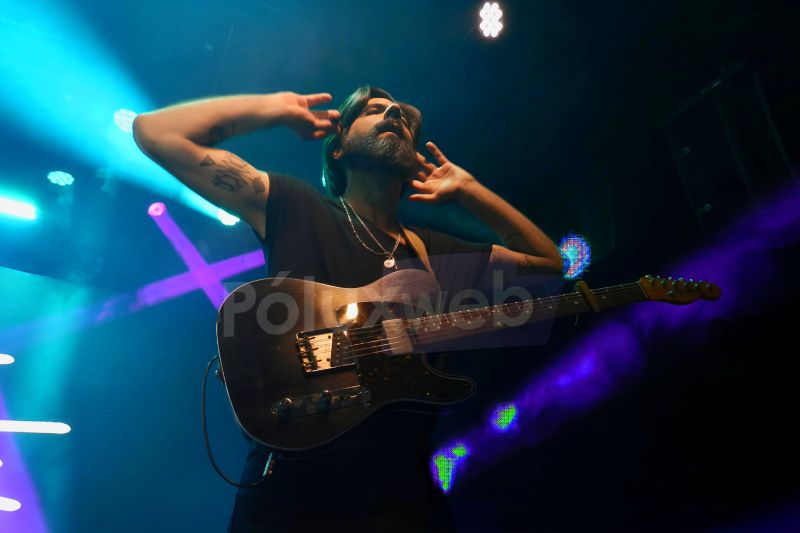 Guitarrista con manos en la cabeza bajo luces rosas y azules.