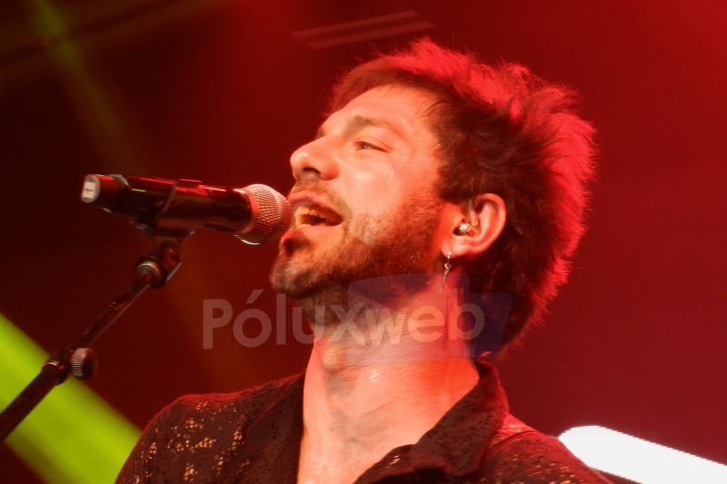 Vocalista cantando bajo luces rojas y amarillas.