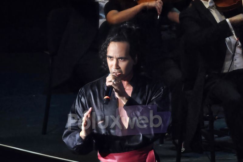Luigi Vidal en Interpretación Solista El cantante Luigi Vidal interpretando apasionadamente un tema con una camisa negra y faja roja en el escenario.