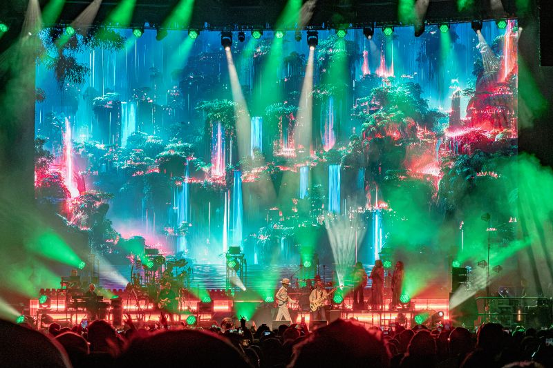 Escenario completo de Jamiroquai con una enorme pantalla de fondo que muestra una selva futurista con cascadas y luces verdes.
