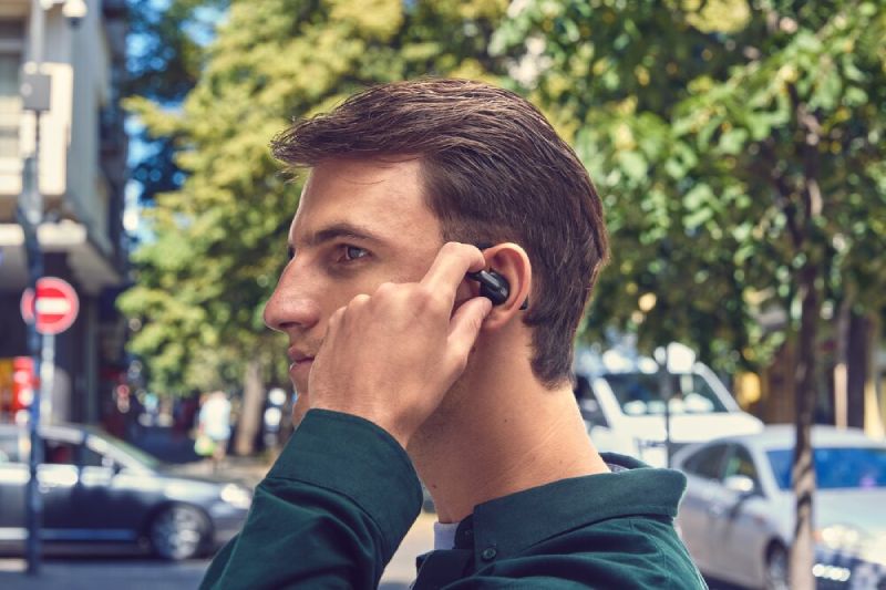 Audífonos inalámbricos JBL Sense Pro con diseño de oído abierto Perfil de un hombre joven caminando en la calle utilizando los audífonos inalámbricos de oído abierto JBL Sense Pro de color negro ajustados sobre su oreja.