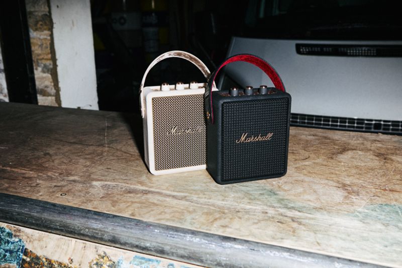 Marshall Stockwell III – Altavoz portátil Dos altavoces portátiles Marshall, uno en color crema y otro en negro, colocados sobre una superficie de madera en un entorno industrial.